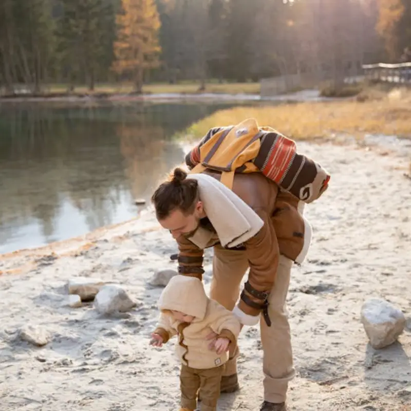 Father helping toddler walk by a lake.